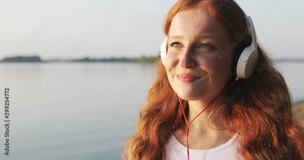 Close up face of redhead freckled girl with white headphones is listening songs and smiling. Close up face of redhead freckled girl with white headphones is listening songs and smiling.