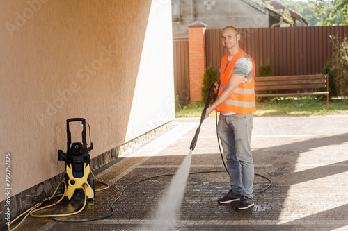 A man in an orange vest cleans a tile of grass in his yard near the house. High pressure cleaning