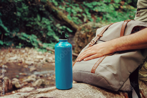 Hiker man sitting with backpack and bottle of water on nature.