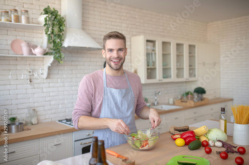 Handsome blue-eyed man feeling cheerful while cooking