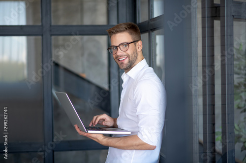Cheerful bearded businessman holding laptop feeling cheerful
