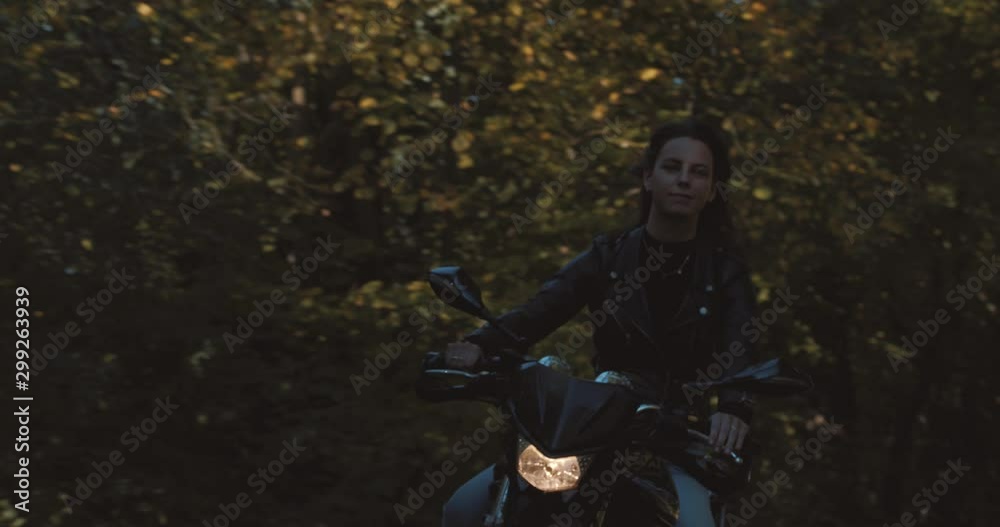 Front view of beautiful European Female motor Biker wearing leather jacket On road with autumn leaf colored Trees at amelisweerd forest on sunny day. Slow Motion in Utrecht, Netherlands
