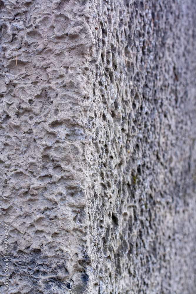 Texture corner of an old concrete wall with holes, hollows with green moss. The porous surface is gray. Selective focus, blurred background.