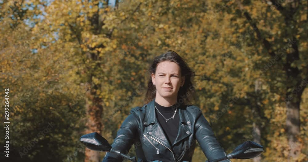 Moving view of pretty smiling European young woman driving a motorbike wearing leather jacket in forest with vibrant, colorful golden autumn leaves on sunny day. Slow Motion, Utrecht , Netherlands Moving view of pretty smiling European young woman driving a motorbike wearing leather jacket in forest with vibrant, colorful golden autumn leaves on sunny day. Slow Motion, Utrecht , Netherlands
