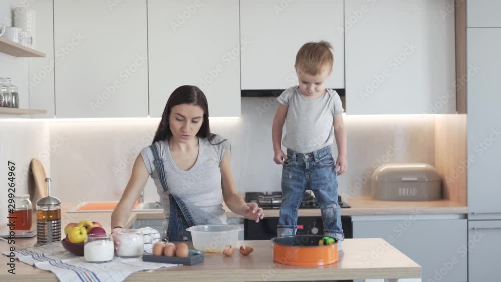 Young pregnant mother breaking eggs into baking mix while son stands on kitchen top Young pregnant mother breaking eggs into baking mix while son stands on kitchen top