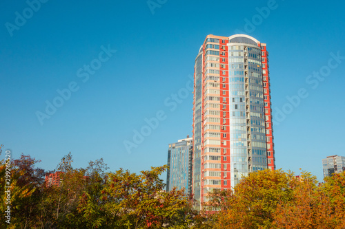 Skyscraper or flat block building on clear blue sky and autumn trees background. Closeup view with copy space. Modern urban architecture landscape