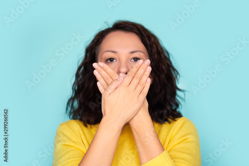 Young woman covering her mouth with her hands, close-up. Silence woman. on a blue background