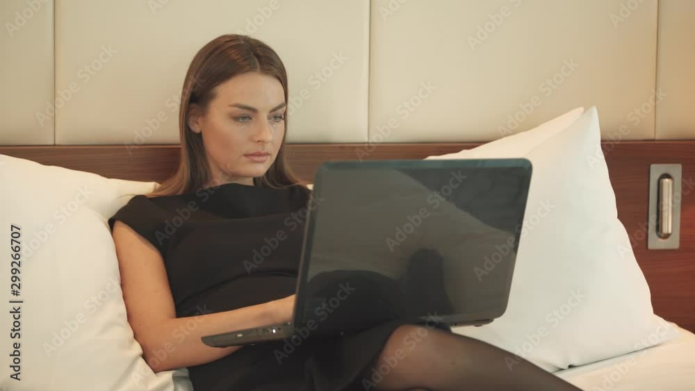 Young female working at a laptop, woman lying on the bed in the hotel, business trip. Young female working at a laptop, woman lying on the bed in the hotel, business trip.
