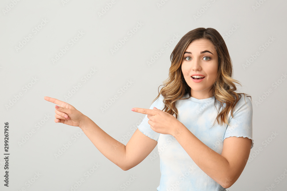 Surprised young woman pointing at something on light background Surprised young woman pointing at something on light background