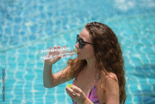 Beautiful girl in a bathing suit is drinking water from a bottle	