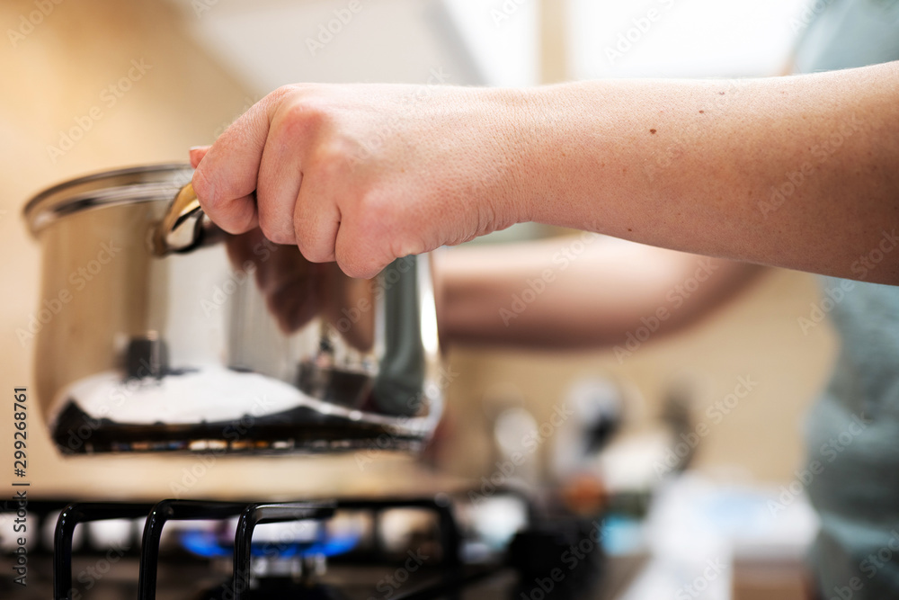 Beautiful young woman housewife prepairing dinner, hold in hands big steel saucepan, standing it on gas-stove. Beautiful young woman housewife prepairing dinner, hold in hands big steel saucepan, standing it on gas-stove.