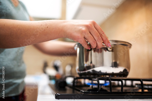 Beautiful young woman housewife prepairing dinner, hold in hands big steel saucepan, standing it on gas-stove.