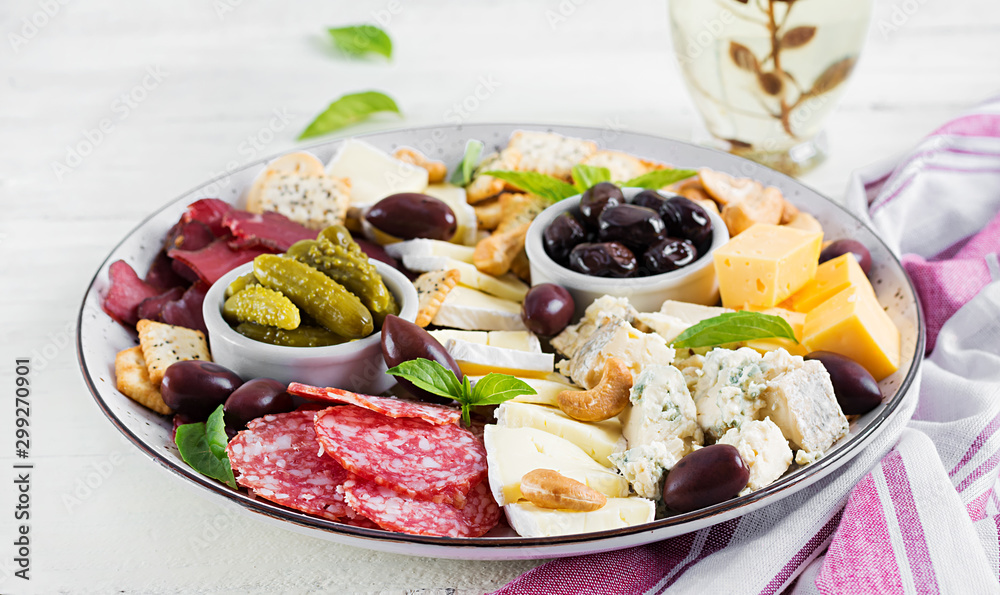 Antipasto platter with basturma, salami, blue cheese, nuts, pickles and olives on a white wooden background.