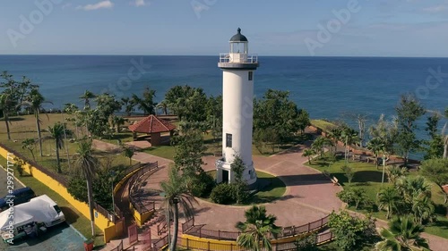 Drone footage of  beautiful white lighthouse surrounded by ocean and Palm trees. photo