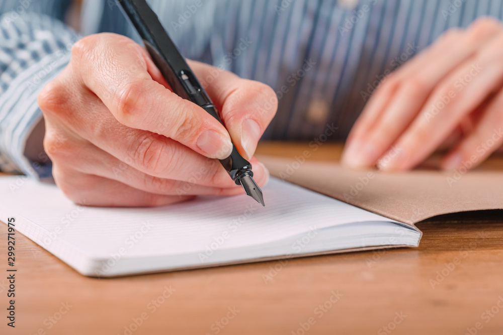Beautiful Female hands write pen in a notebook of tasks and goals to work on a wooden table Beautiful Female hands write pen in a notebook of tasks and goals to work on a wooden table