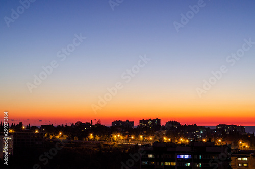 Picturesque pink sunset over the city with silhouettes of houses. House lights and street lamps. The gradient of the sky, from blue to red. Evening panorama of the city. Cozy cityscape from above. Cop