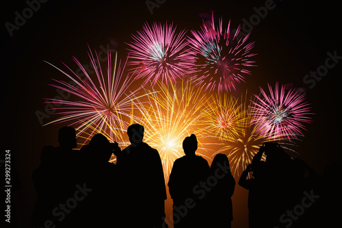 Crowd watching fireworks and celebration. Happy family sitting on floor and watching the fireworks Celebration at night on New Year and copy space - abstract holiday background.