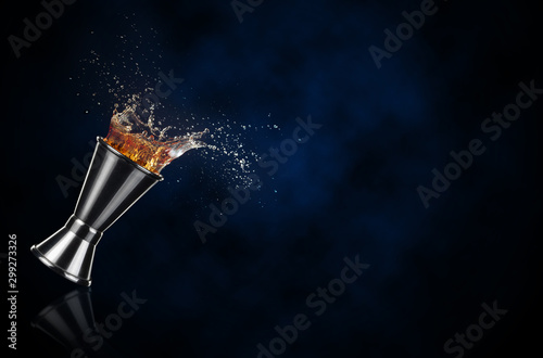 brown liquor splashing out of a jigger isolated on dark blue background.