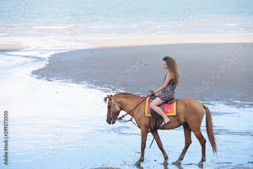 A pretty woman in a bikini is happily riding a horse on the beach.