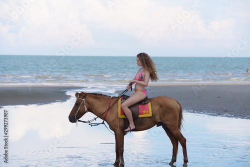 A pretty woman in a bikini is happily riding a horse on the beach. © tharathip