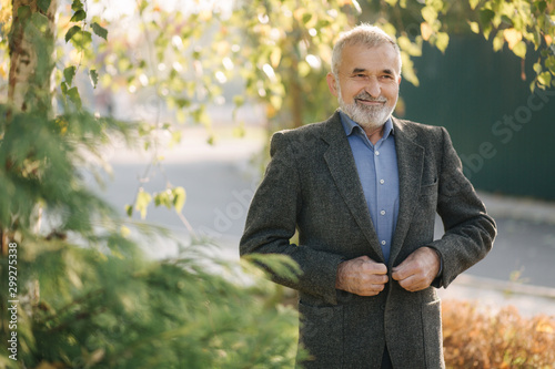 Portrait of happy elderly man in the park. Gray-haired bearded man in gray jacket