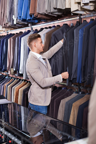 Young man choosing new suit in men’s cloths store