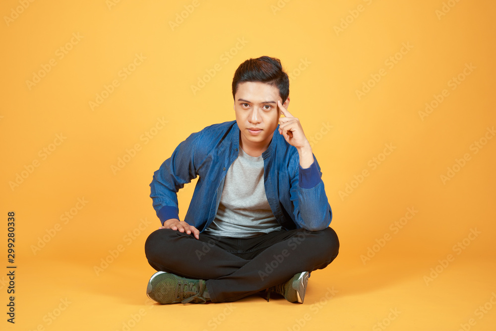 Young Aisan man sitting and thinking something isolated on colore orange background. Young Aisan man sitting and thinking something isolated on colore orange background.