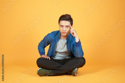 Young Aisan man sitting and thinking something isolated on colore orange background. © makistock