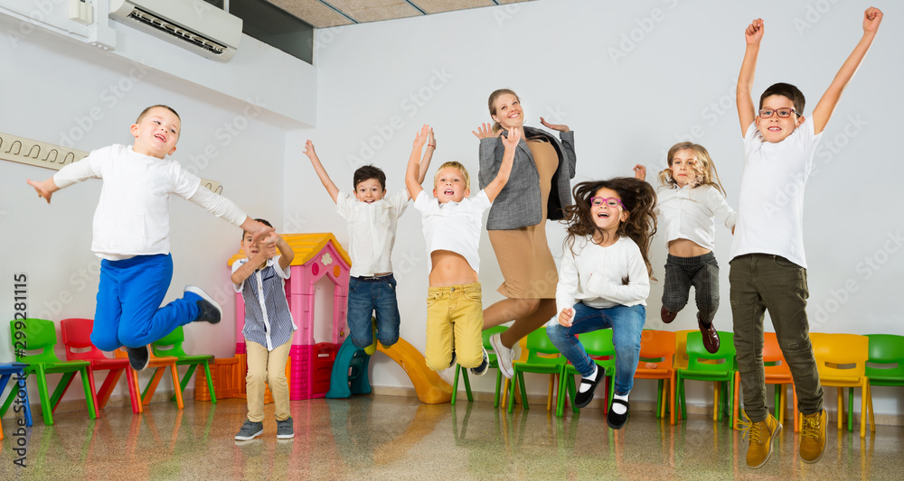 Fototapeta premium Children with teacher jumping together in schoolroom