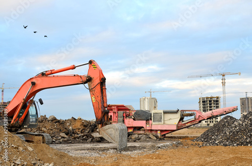 Heavy tracked excavator load stone, old asphalt or concrete waste into a mobile jaw crusher machine. Crushing and processing into gravel for recycling in concrete or cement production.