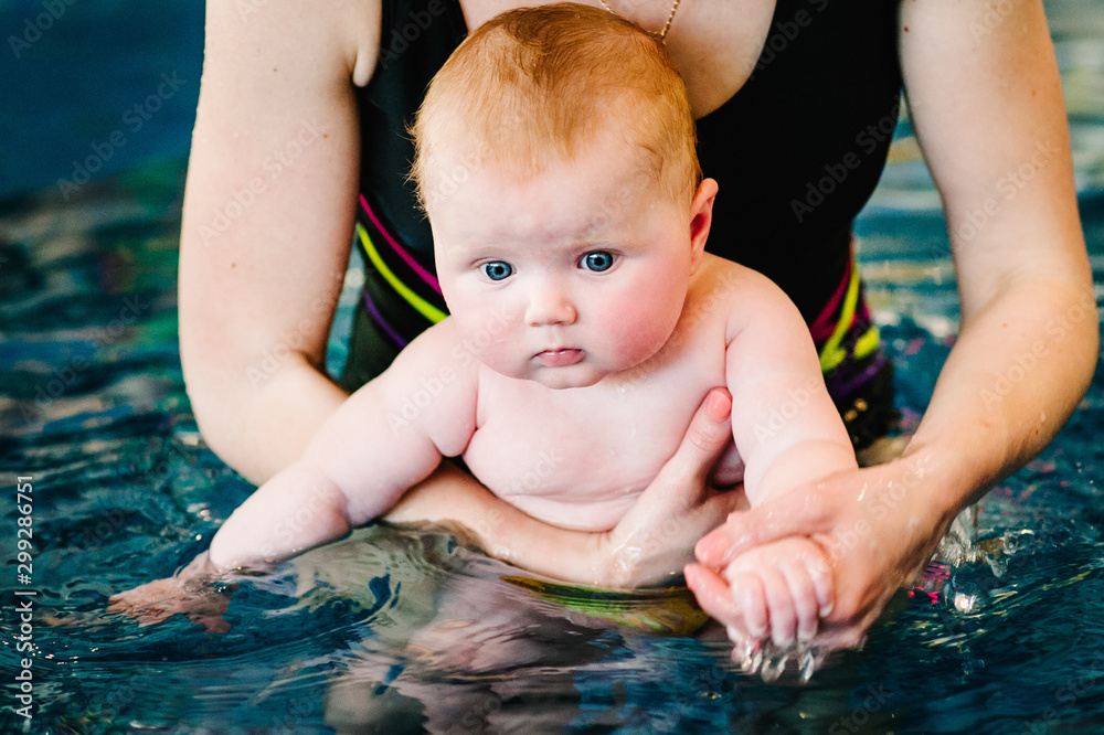 Enjoy the first day of swimming in the water. Mom holds child preparing for diving. doing exercises. Young mother, swimming instructor and happy little girl in the pool. Teaches infant child to swim Enjoy the first day of swimming in the water. Mom holds child preparing for diving. doing exercises. Young mother, swimming instructor and happy little girl in the pool. Teaches infant child to swim