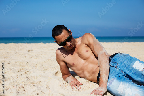 young muscular man resting and posing on the beach