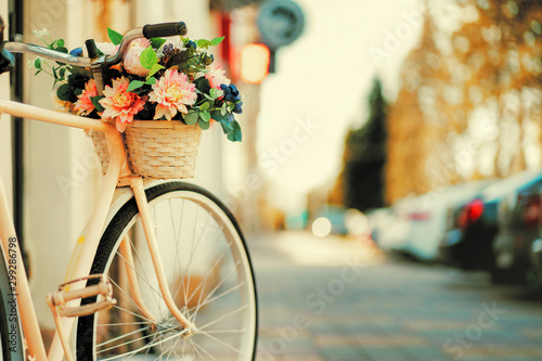 Fotobehang Witte fiets met een mand met bloemen die bij de deur op straat  in de stad staat - Nikkel-Art.be