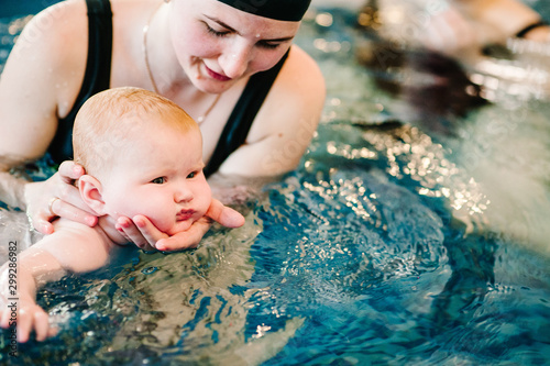 Young mother, happy little girl in the pool. Teaches infant child to swim. Enjoy the first day of swimming in water. Mom holds child preparing for diving. doing exercises. hand leading child on water