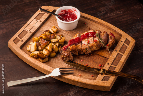 Grilled meat served with potatoes and sauce on an wooden board. The festive dinner from chief-cooker.