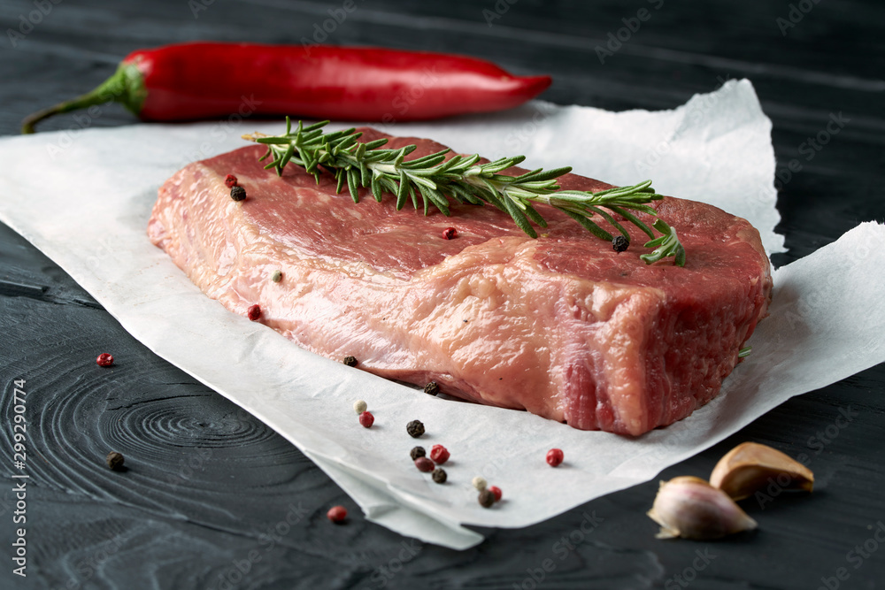 Raw fresh meat on paper with herbs, pepper and garlic on dark background