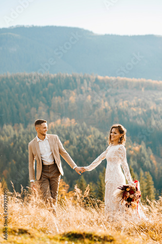 Lovely gorgeous bride and groom walking in sun light holding hands, boho wedding couple