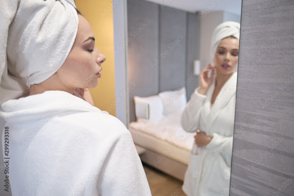 Obraz premium Close up of body of young woman tying up belt of white bathrobe in front of the mirror