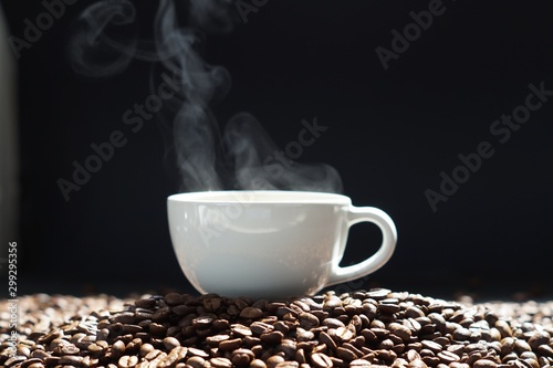 a cup of hot coffee with steaming and beans on wooden and black background