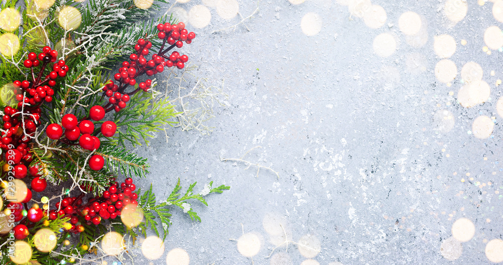 Christmas or winter background with a border of green and frosted evergreen branches and red berries on a grey vintage board. Flat lay - obrazy, fototapety, plakaty 