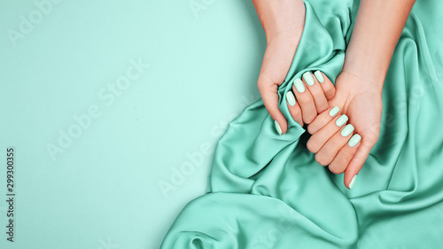 Hands of a young girl on a mint silk cloth, manicure on a trendy background , green polish photo