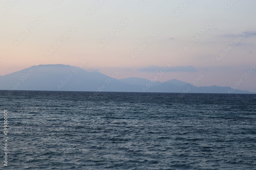 wavy sea with rocks and mountains in background