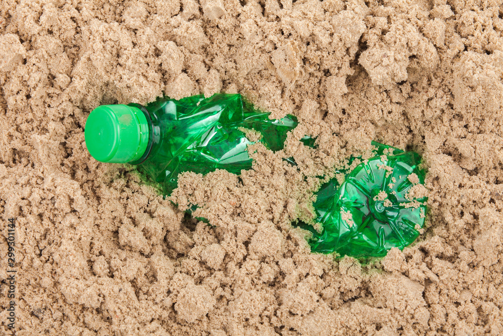 A crushed green bottle almost buried in sand A crushed green bottle almost buried in sand
