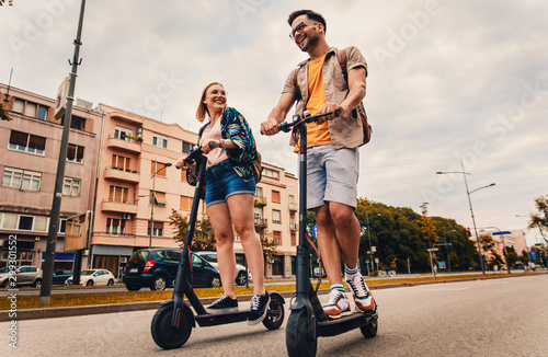 Young couple on vacation having fun driving electric scooter through the city. photo