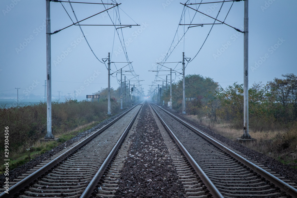 Two train tracks leading into distance. Poles with power lines overhead. Very moody and grey atmosphere. Efficient and fast way of transport. Two train tracks leading into distance. Poles with power lines overhead. Very moody and grey atmosphere. Efficient and fast way of transport.