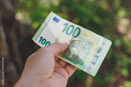 Male hand holding 100 hundredth euro banknote on green background photo