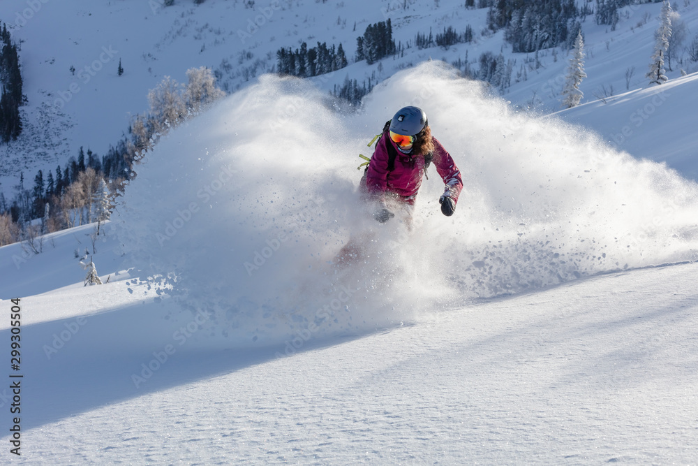 freerider in a bright suit rides fast skiing with large splashes of snow on a sunny day. Young Beautiful female skier. Snow scoot. Extreme winter sports. sunrise light, edit space. 