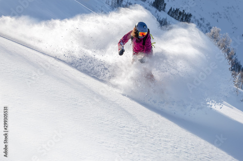 female snowboarder curved and brakes spraying loose deep snow on the freeride slope. downhill with snowboards in fresh snow. freeride world champion. swirls of snow in the air  in a bright mask