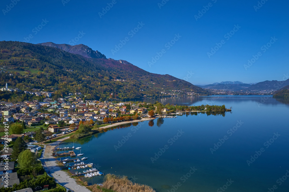 Aerial view of Lake Caldonazzo north of Italy. In the background the trees, Alps, blue sky. Reflection of mountains in water. Autumn season. Multi-colored palette of colors