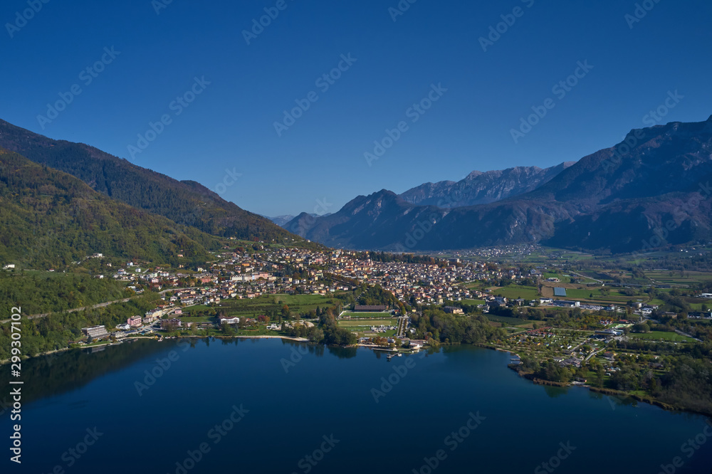 Aerial view of Lake Levico north of Italy. In the background the trees, Alps, blue sky. Reflection of mountains in water. Autumn season. Multi-colored palette of colors